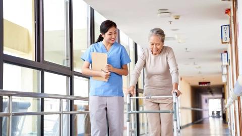 Eine Pflegerin begleitet eine Seniorin mit Gehhilfe.