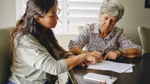 Eine Frau hilft einer älteren Frau dabei Dokumente zu sortieren. 