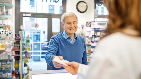 Mann reicht Apothekerin ein Rezept.