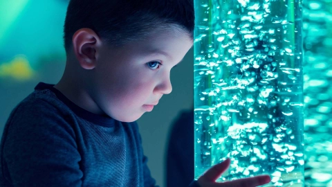 Ein Junge lehnt sich mit der Stirn an eine erleuchtete Wassersäule.