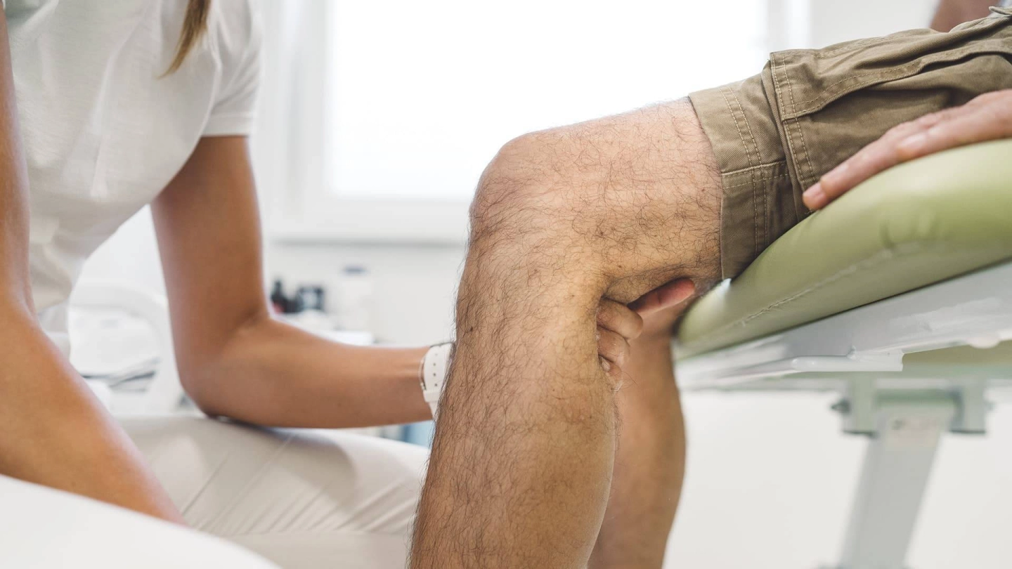 Eine Ärztin untersucht die Kniekehle eines Patienten.