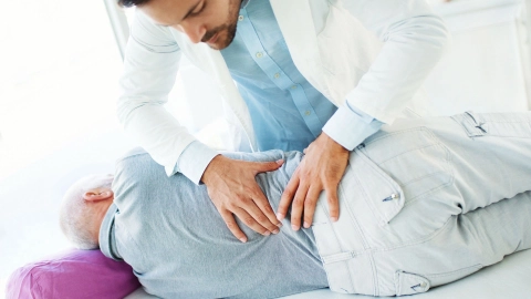 طبيب يفحص قرصًا فقريًا لرجل يستلقي على جانبه على سرير.