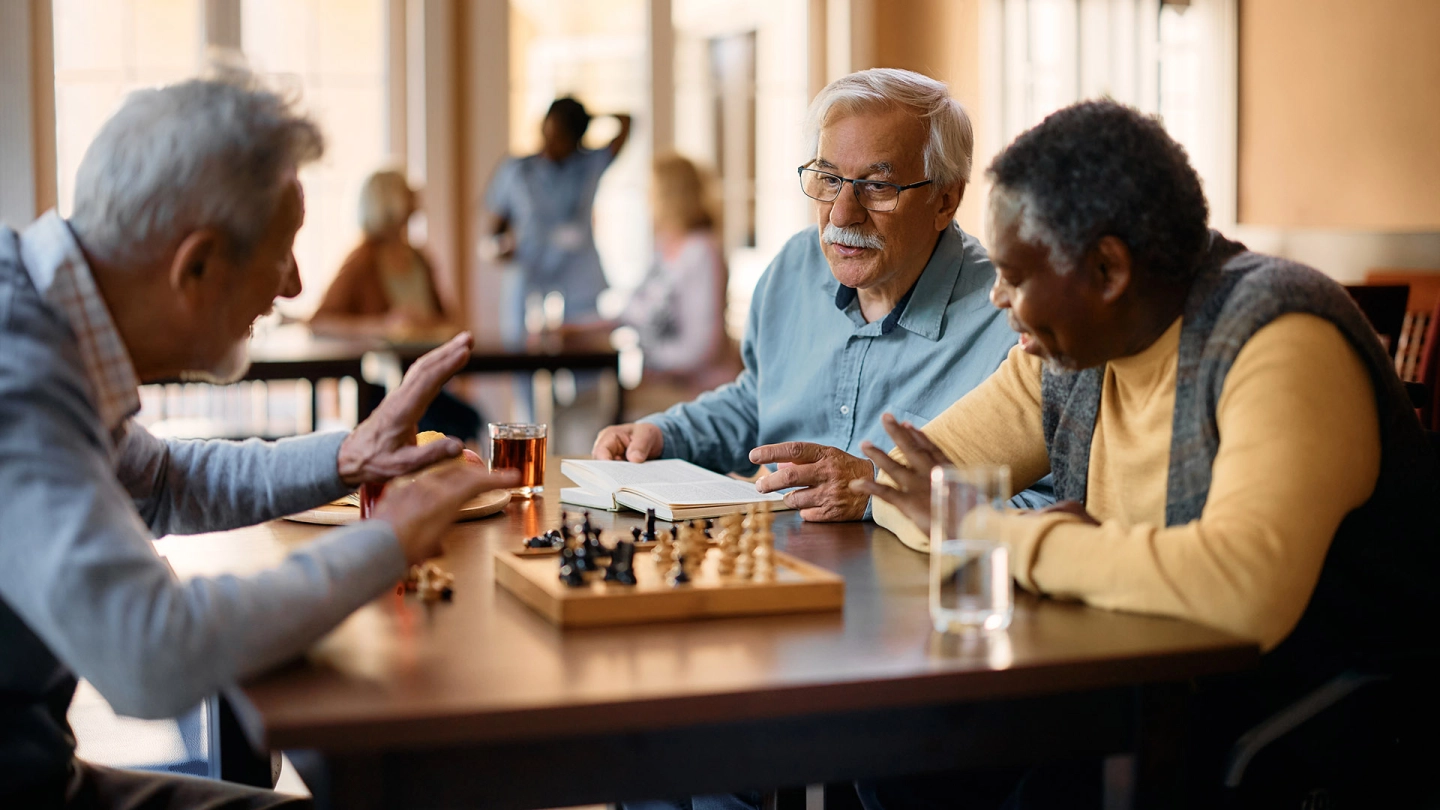 كبار سن من الرجال يلعبون الشطرنج في المنطقة المشتركة.