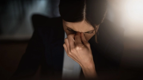 Burn-out: Eine Frau mit gesenktem Kopf fasst sich zwischen Nase und Stirn.