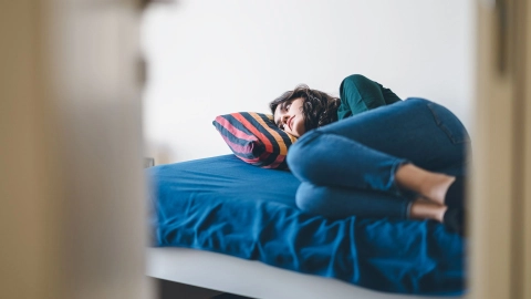 Eine depressiv wirkende Frau liegt auf einem Bett und blickt ins Leere.