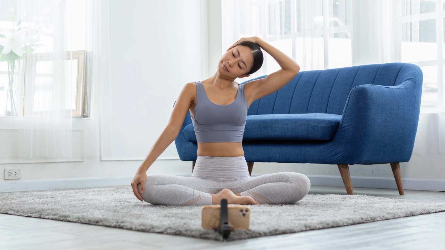 Eine Frau sitzt auf dem Boden vor ihrem Smartphone und macht Entspannungs- und Dehnungsübungen. 