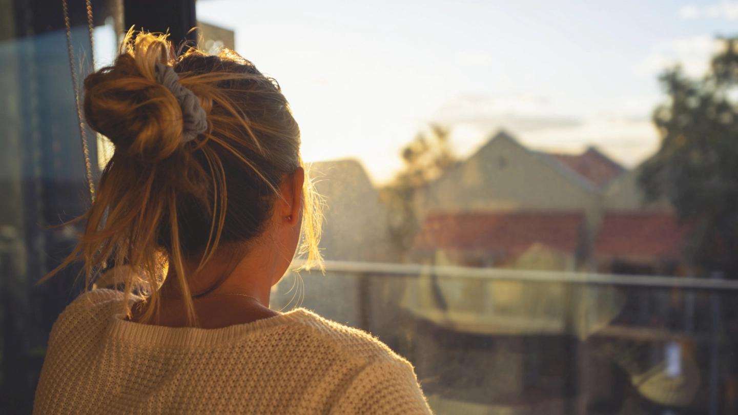 Eine junge Frau schaut bei Sonnenuntergang durch das Fenster.