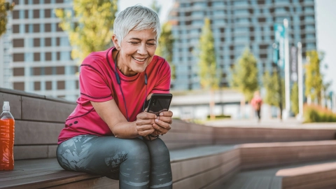 Eine Frau sitzt auf einer Holzbank und schaut auf ein Smartphone.