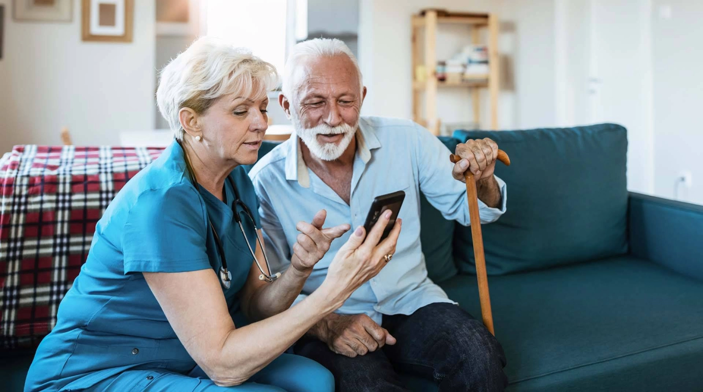 Pflegerin zeigt älterem Mann etwas auf dem Smartphone.