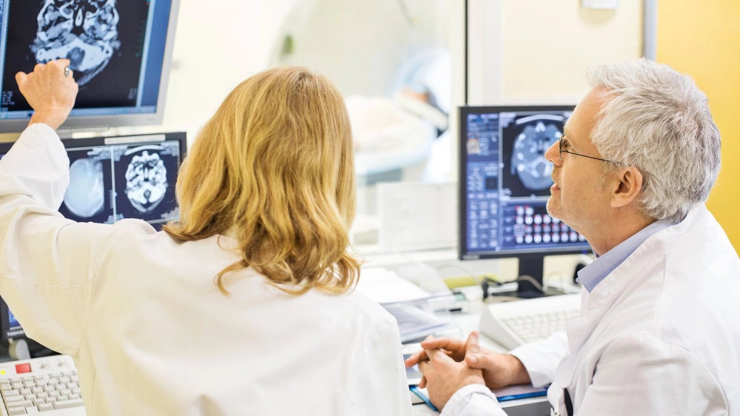 Epilepsie: Eine Ärztin und ein Arzt begutachten das gescannte Bild eines Schädels und Gehirns auf einem Monitor.