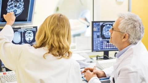 Epilepsie: Eine Ärztin und ein Arzt begutachten das gescannte Bild eines Schädels und Gehirns auf einem Monitor.