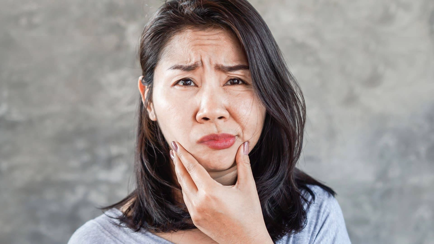 امرأة تمسك بذقنها وتنظر بجدية إلى الكاميرا. ويبدو الجانب الأيمن من وجهها ممدودًا وفمها يبدو معوجًا.