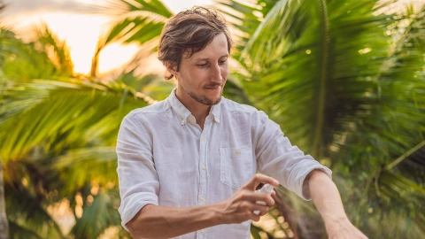 Junger Mann sprüht Mückenspray auf den Unterarm.