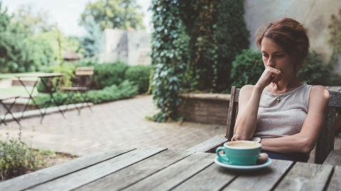 امرأة تجلس على طاولة في حديقة، وتضع رأسها على يدها وتنظر إلى الطاولة. ويبدو أنها قلقة.