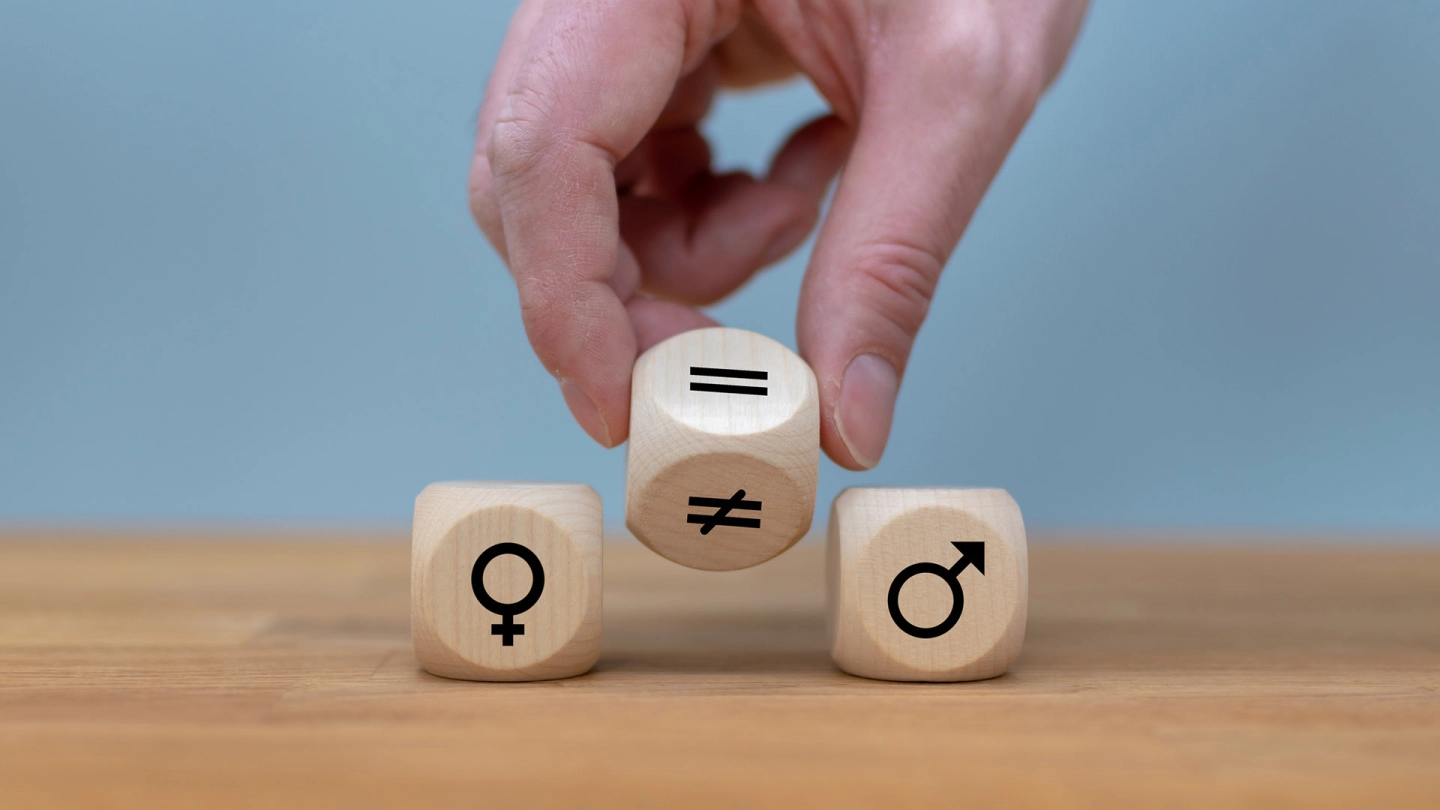 A die with an equal sign and an unequal sign is placed between two dice with symbols for female and male.