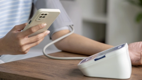 Eine Person misst ihren Blutdruck und schaut dabei auf ihr Smartphone.