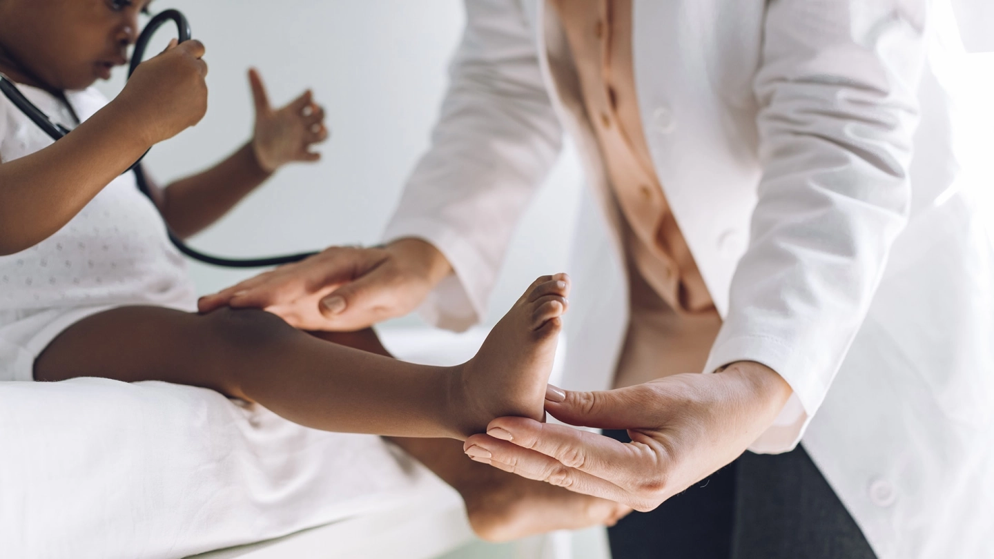 Medical examinations for children and adolescents: small child sitting on a doctor’s couch playing with a stethoscope. A doctor is examining the child carefully.