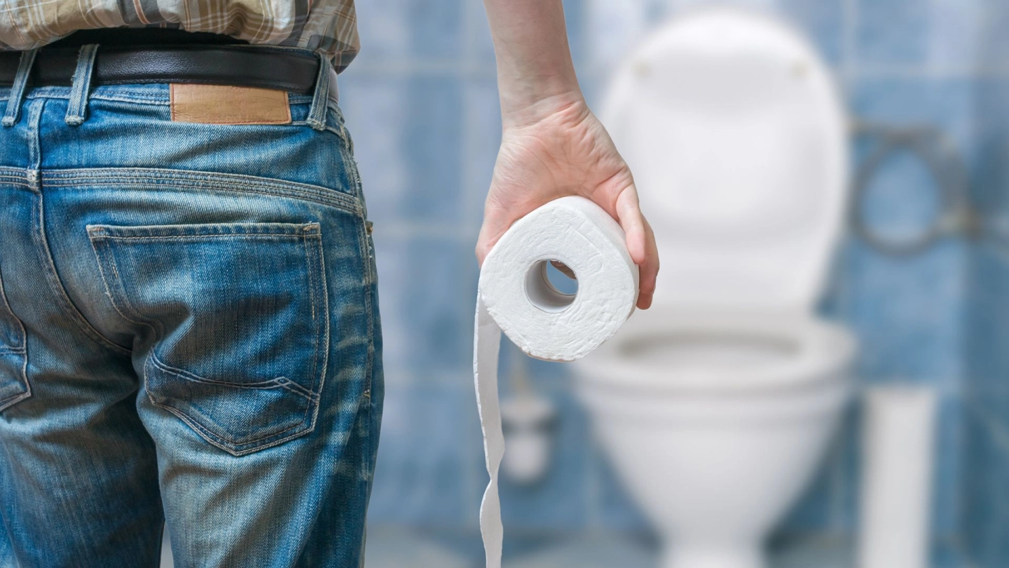 Ein Mann steht mit Toilettenpapier vor einer Toilette