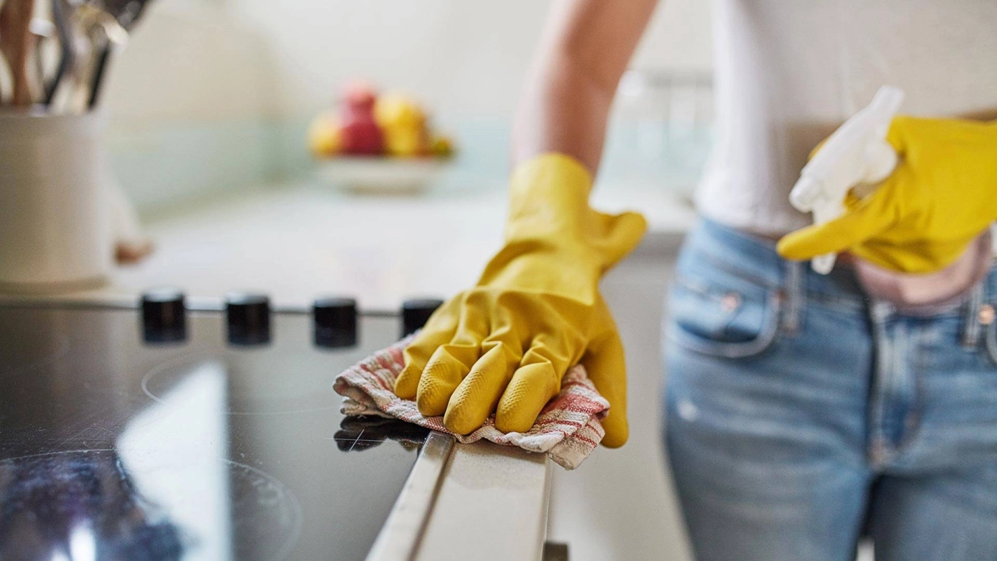 Eine Person mit Haushaltshandschuhen poliert mit einem Lappen den Herd.