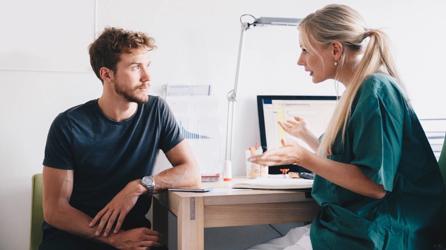 سرطان الخصية: رجل يجلس في غرفة العلاج. وينظر إلى طبيبة تجلس أمامه ويتحدث معها.