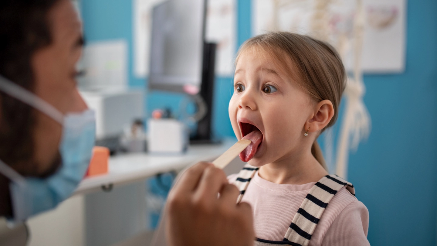 A doctor examining a girl’s throat with a wooden spatula.