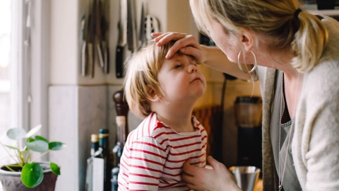 Hornhautnarben und Hornhauttrübungen: Eine Frau steht vor einem kleinen Jungen und berührt ihn mit einer Hand an der Stirn. Dabei schaut sie dem Jungen in ein Auge.