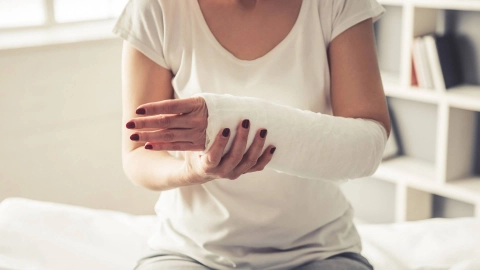 Nahaufnahme einer Frau mit geschientem Unterarm, die auf einer Behandlungsliege sitzt.