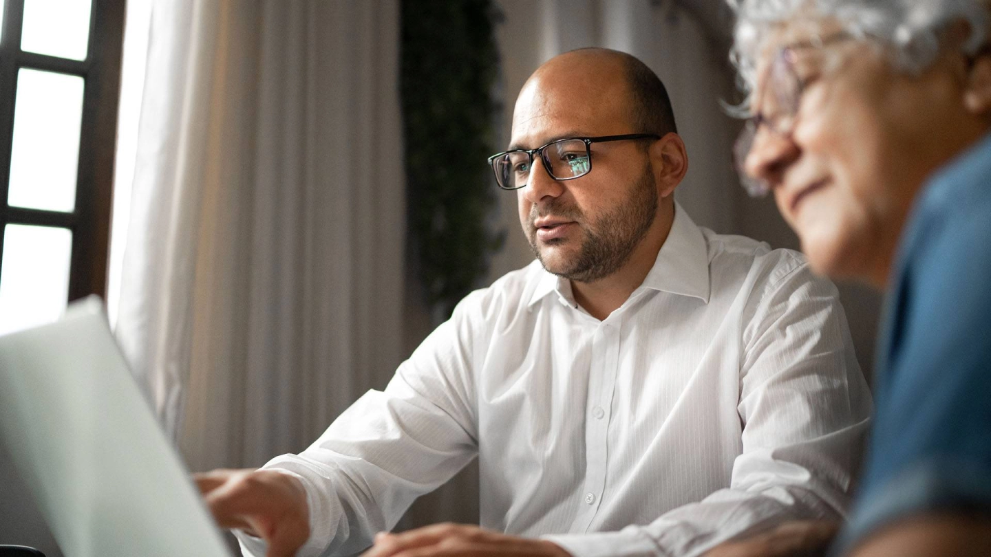 Ein Mann informiert sich am Computer, eine ältere Frau schaut ihm neugierig über die Schulter.