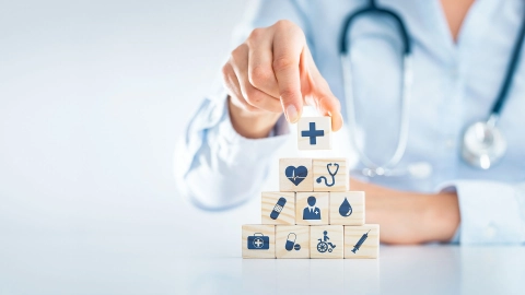 Eine Person mit Stethoskop stapelt Würfel mit Gesundheits-Symbolen. 