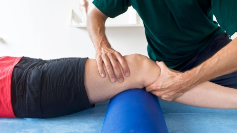 Физиотерапевт проводит лечение коленного сустава пострадавшего мужчины.