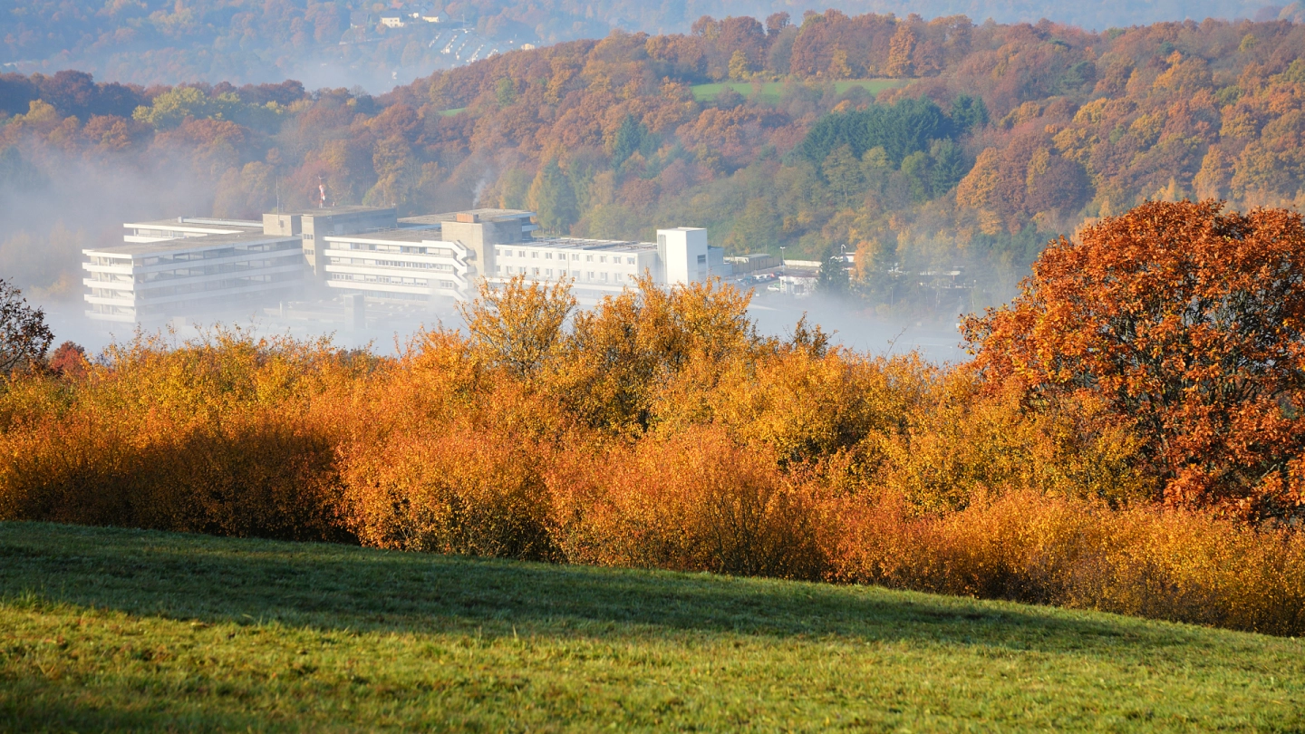 Modernes Krankenhausgebäude zwischen bewaldeten Hügeln.