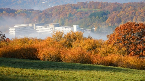 Modernes Krankenhausgebäude zwischen bewaldeten Hügeln.