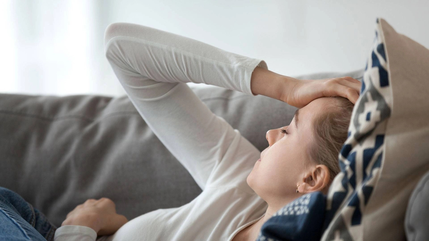 Молодая женщина без сил лежит на диване.