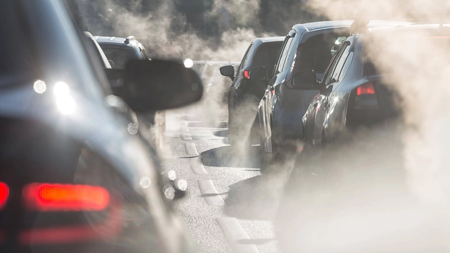 Nahaufnahme von Autos im stockenden Verkehr und Abgaswolken.