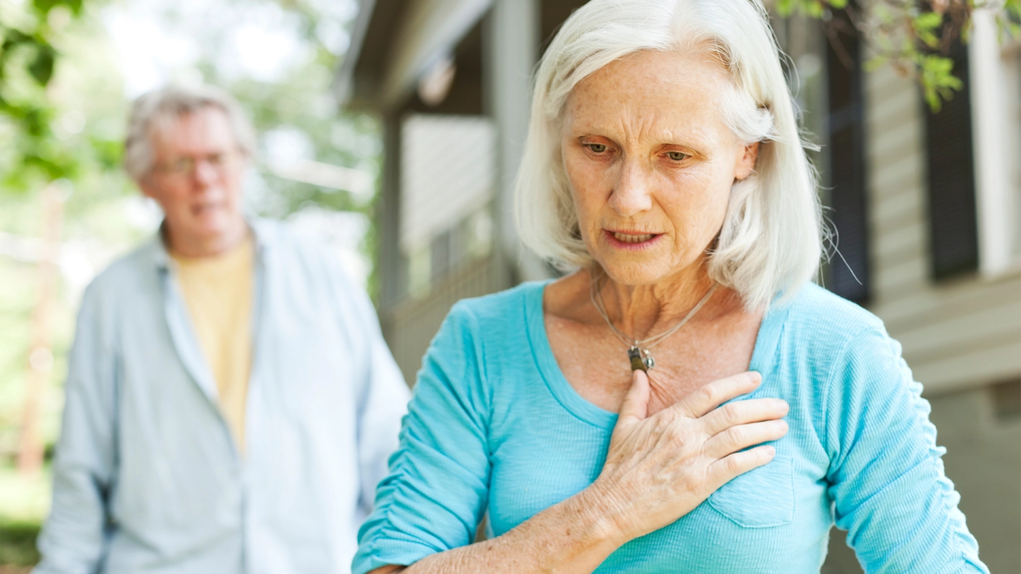 An elderly woman holds a hand to her chest.