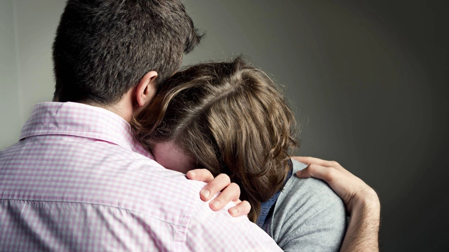 Bir kadın başını bir erkeğin omzuna yaslıyor. Kadın yüzünü erkeğin göğsünde gizliyor. Kadın umutsuz görünüyor.