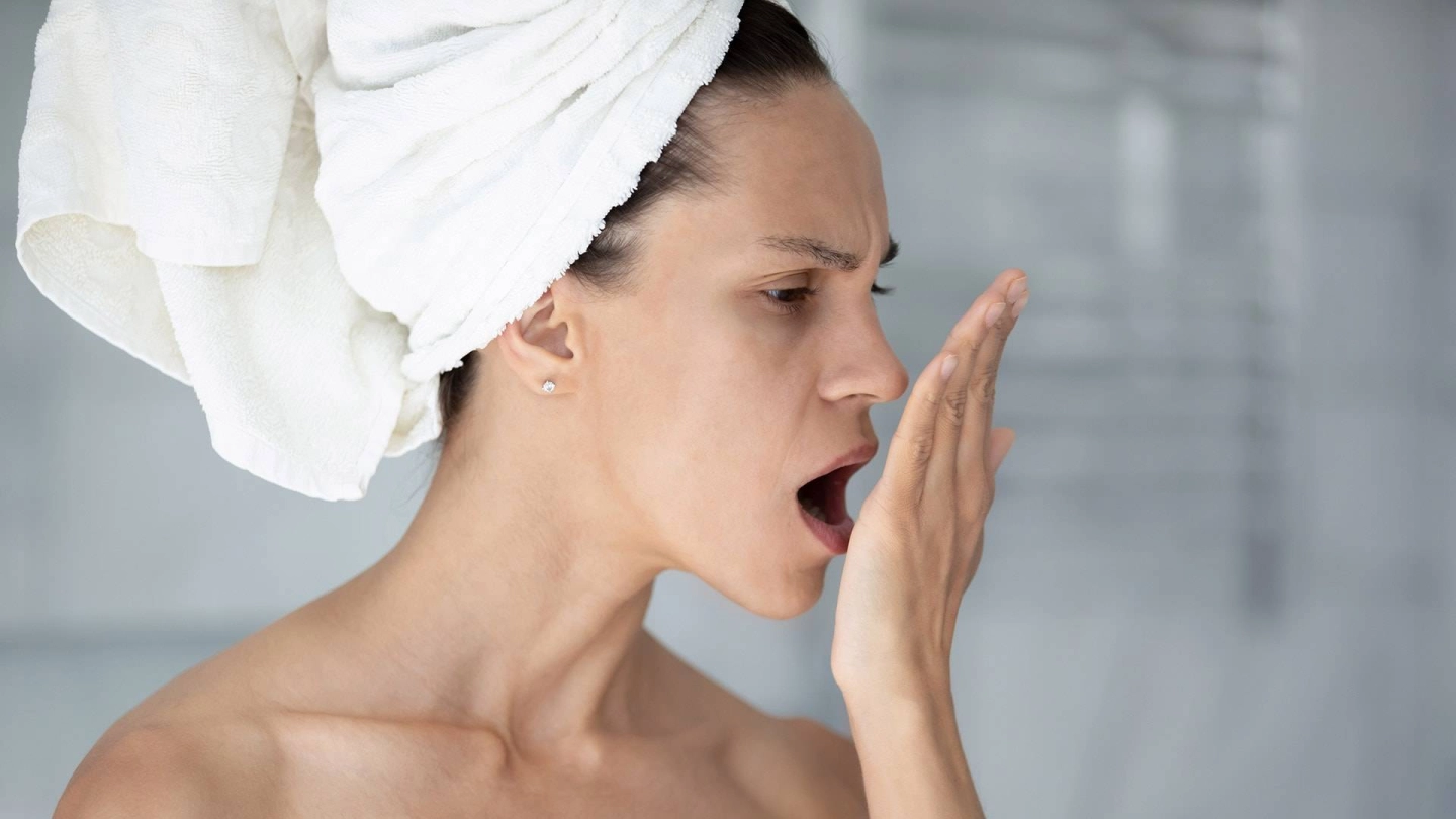 Eine Frau mit um den Kopf gewickeltem Handtuch haucht in ihre offene Hand, um den Atem zu prüfen.