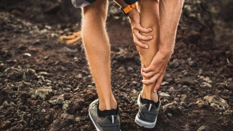 Eine Person in Sportkleidung bückt sich und fasst sich an die vermutlich schmerzende Wade.