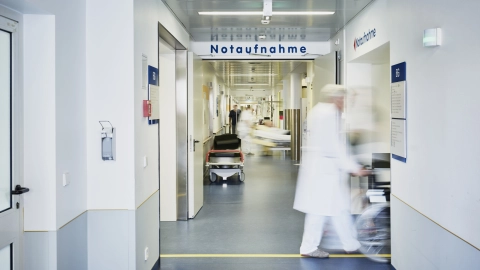 Krankenhauspersonal schiebt einen Patienten im Rollstuhl über den Gang der Notaufnahme