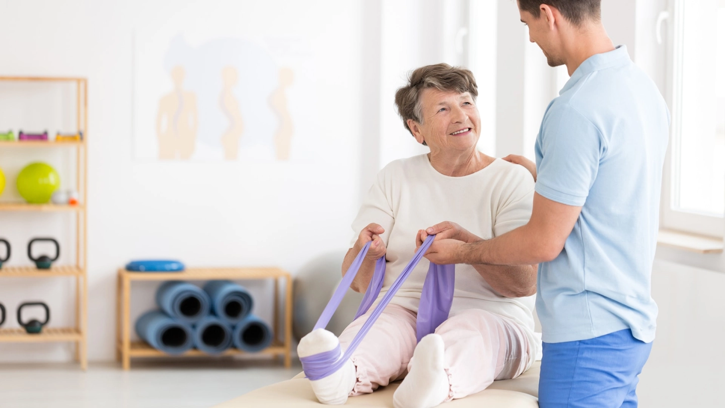 Пожилая женщина делает упражнения с помощью ленты для фитнеса под руководством тренера