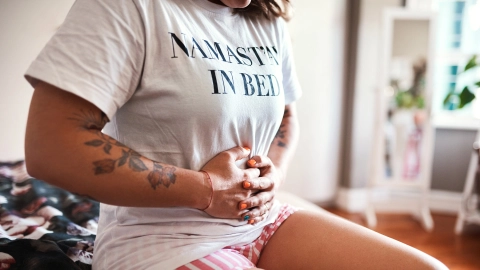 Ovarialzysten: Eine Frau sitzt auf einem Bett und hält sich mit beiden Händen den Bauch.