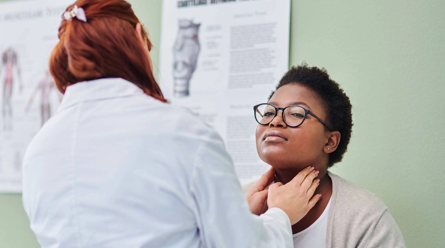 Женщина-врач проводит обследование лимфатических узлов на шее молодой пациентки.