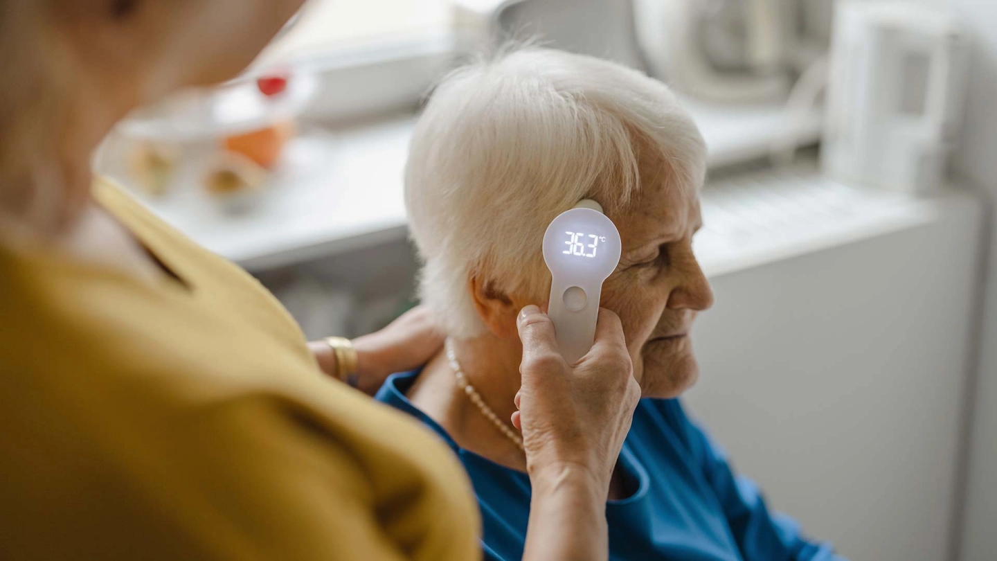 Сиделка измеряет температуру у пожилой женщины.