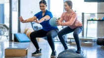 Ein Mädchen macht mit einer Physiotherapeutin Übungen mit einem Ball