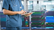 Eine medizinische Fachkraft bedient ein Tablet, im Hintergrund sind Monitore zur Kreislaufüberwachung sichtbar.