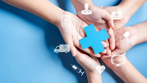 Mehrere Hände liegen übereinander und halten ein Kreuz, das das Gesundheitswesen symbolisiert. Darum herum sind Symbole gruppiert, die für Leistungen der Krankenversicherung stehen. 