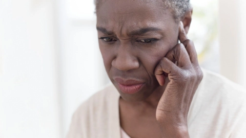 Tinnitus: Eine Frau fasst sich mit einem Finger ans Ohr und schaut skeptisch.
