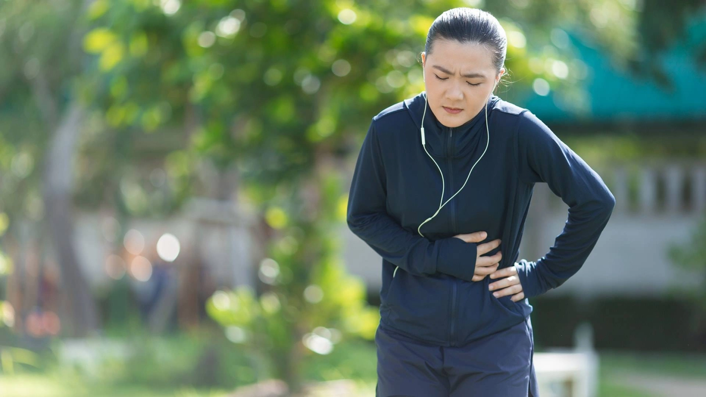 Koşu kıyafetleri içinde genç bir kadın açık havada durmuş ve karnının sol tarafını tutuyor.