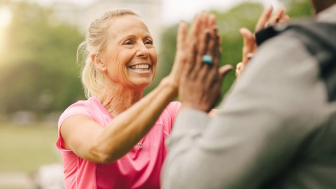 Eine sportliche Frau mittleren Alters klatscht sich mit einer anderen Frau ab.