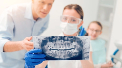 Eine Ärztin, die Mundschutz und Schutzbrille trägt, hält ein Röntgenbild eines Gebisses zur Ansicht der Weisheitszähne in den Händen.